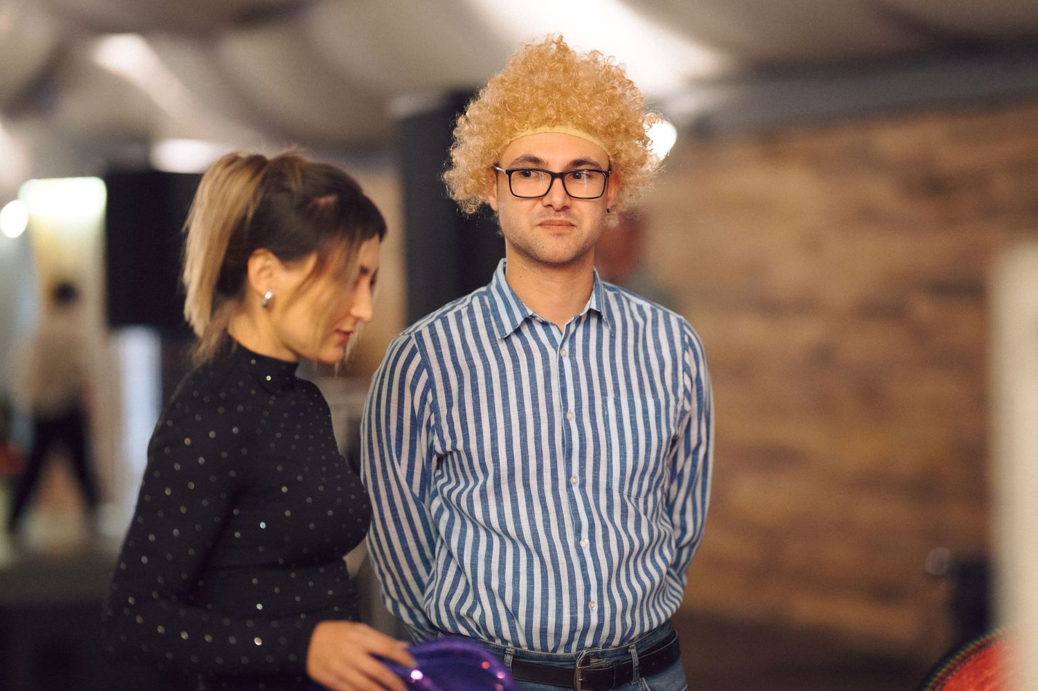Two people chatting in casual setting with brick wall background.
