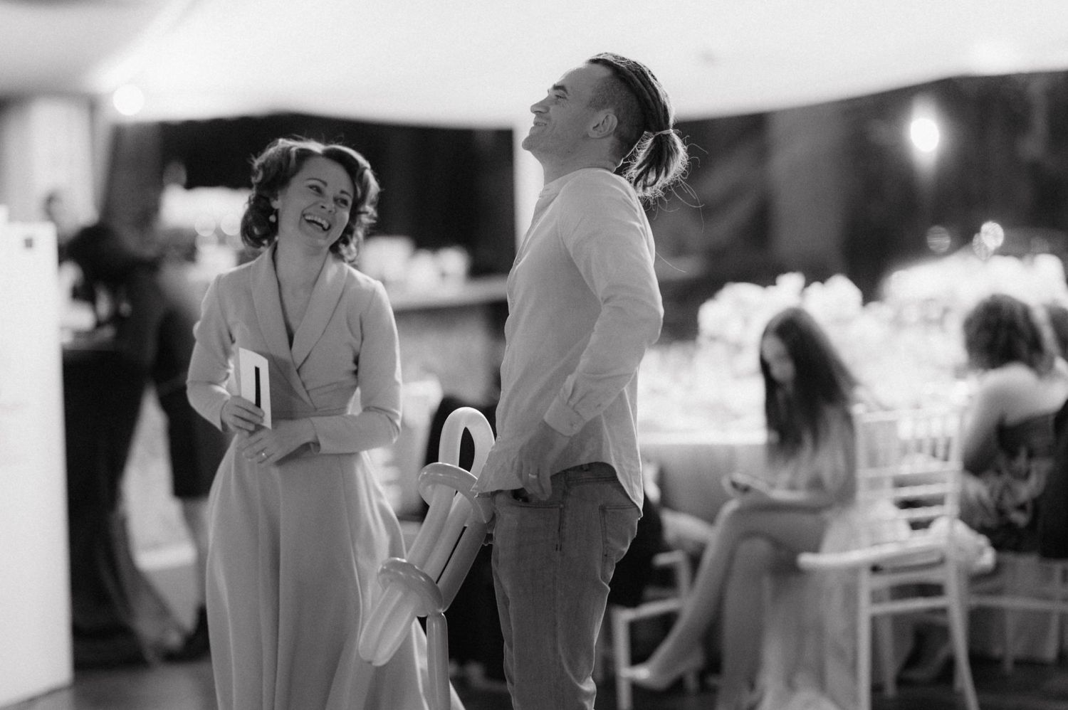 A black and white photo shows two people sharing a laugh during a wedding reception.