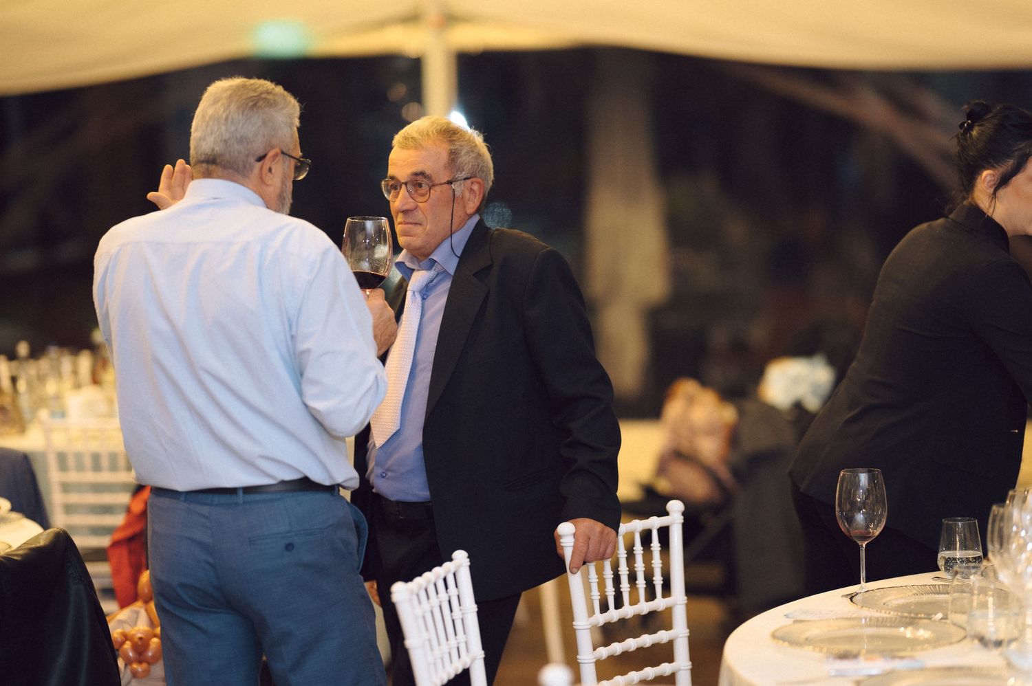 Two older men in formal attire have an animated conversation at an indoor event.