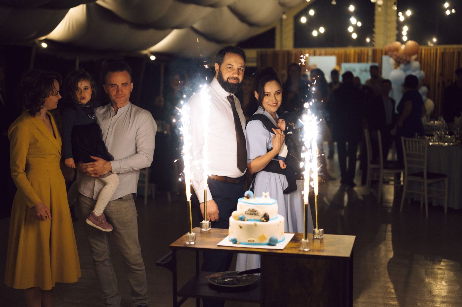 Guests gather around a tiered cake with sparkler fountains at an evening celebration.