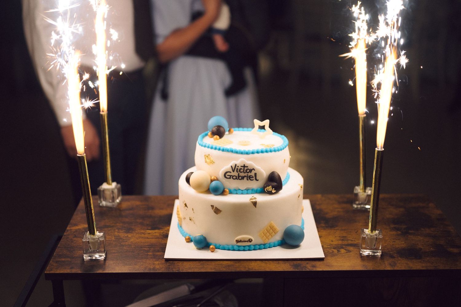 A white tiered cake decorated with blue accents and sparkler fountains on display.