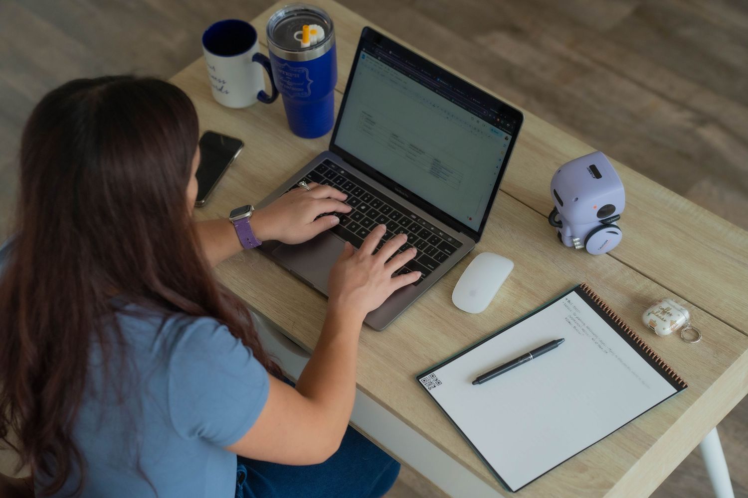 Remote worker using laptop and taking notes at wooden desk with coffee cup and office supplies.
