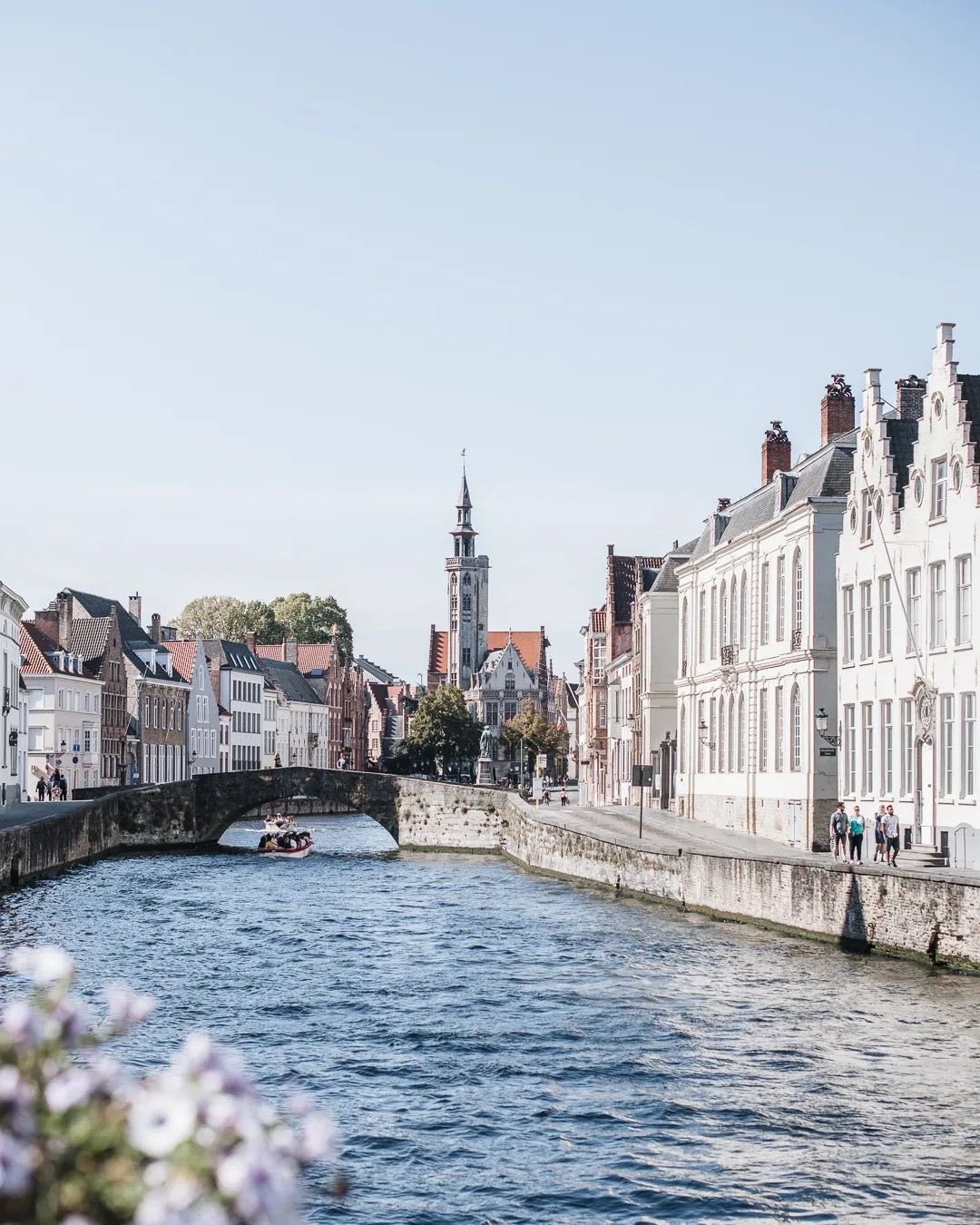 Historic riverside buildings and a small arched bridge over calm water.