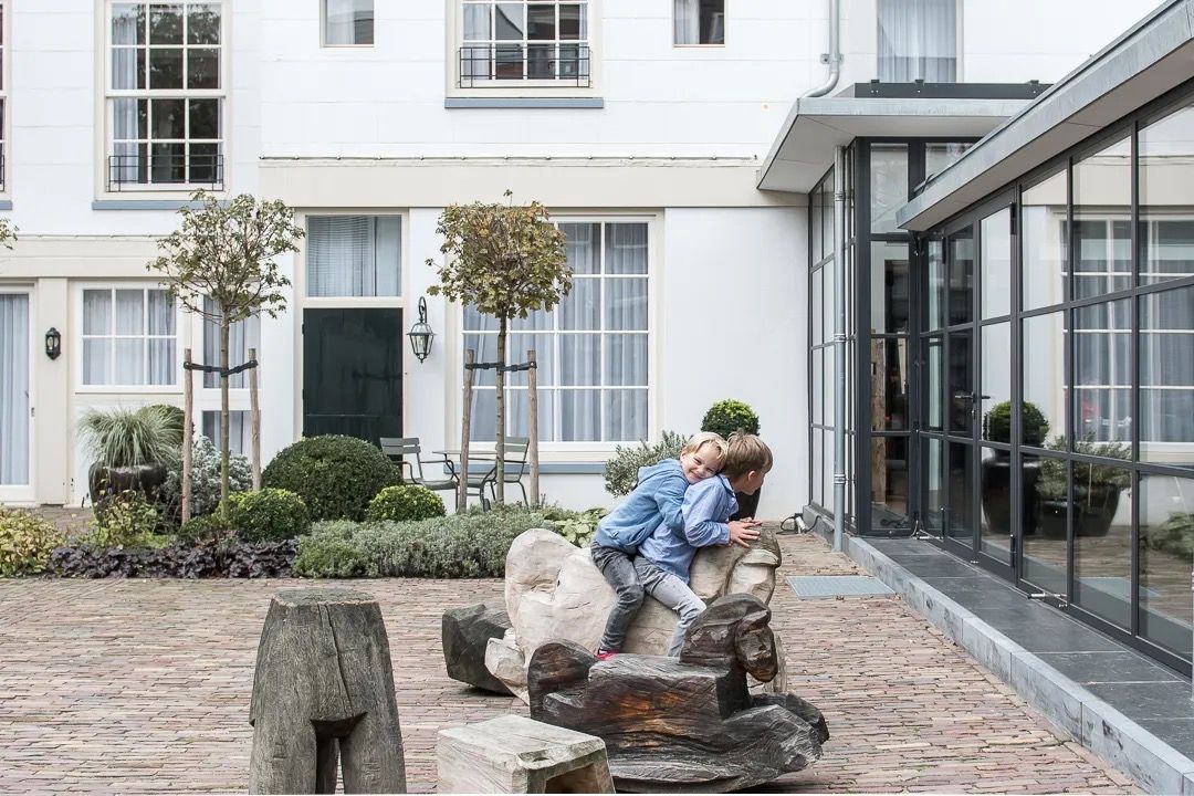 Children playing on a stone sculpture in a quiet Amsterdam courtyard with white townhouses.