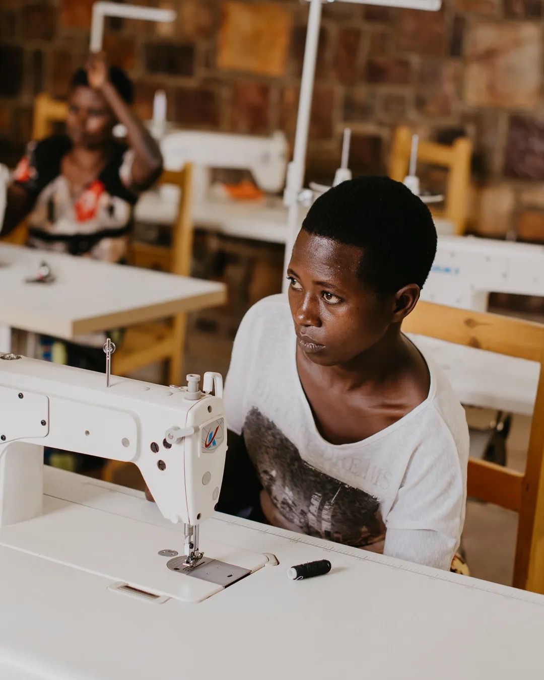 Young girl sits at a sewing machine in a classroom, learning new skills in a supportive education space.