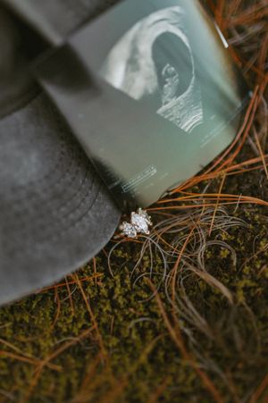 Close-up of a sparkling diamond engagement ring on moss and pine needles.
