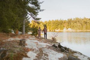 Couple enjoying a romantic sunset by a serene lake surrounded by pine trees.