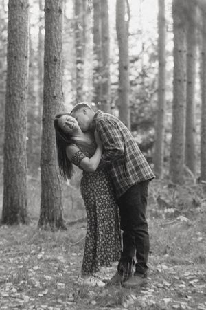 Playful couple photoshoot in a misty pine forest with black and white filter.