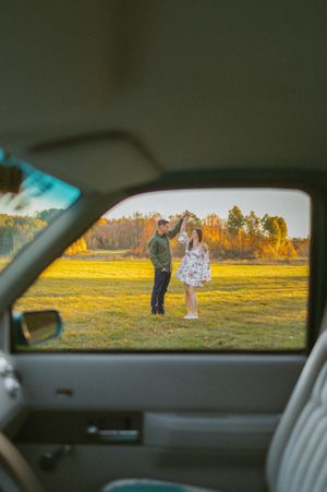 View through car window of golden field at sunset with figures in distance.