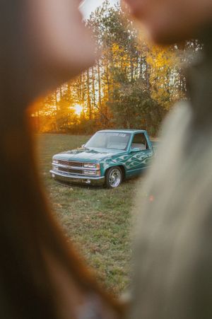 Classic turquoise Chevrolet parked in field during golden hour sunset.