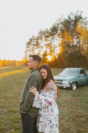 A couple shares an intimate moment in front of a classic truck during golden hour in a rural setting.