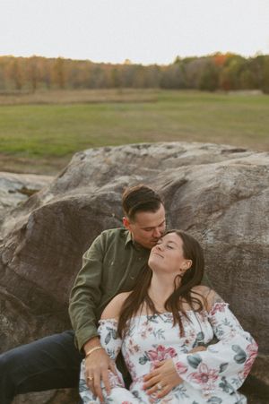 A romantic moment captured on a large boulder during sunset in an open field.