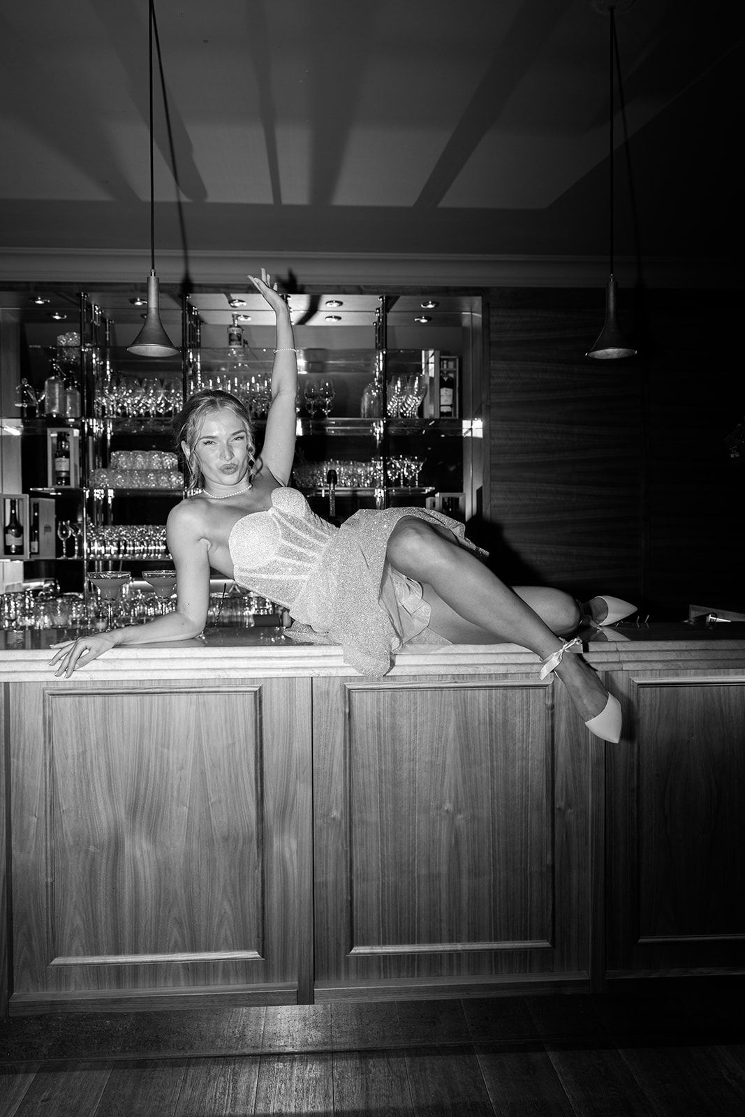 A black and white photo sequence shows a person playfully posing while lying on top of a wooden bar counter.