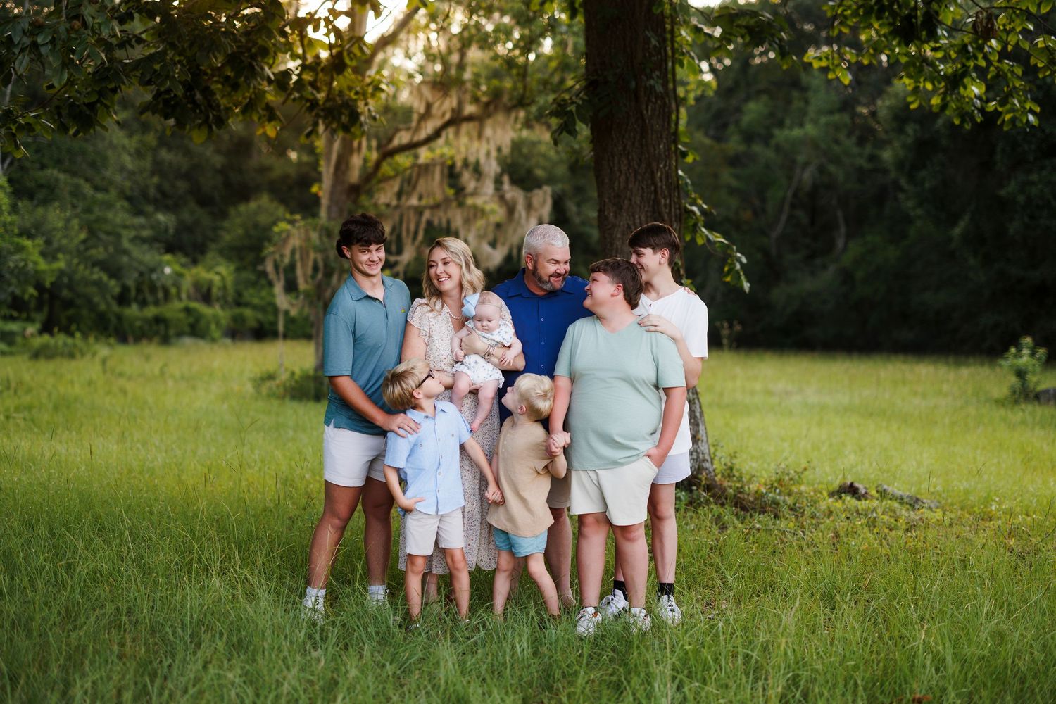 A family group sits together outdoors in a grassy field during golden hour lighting.