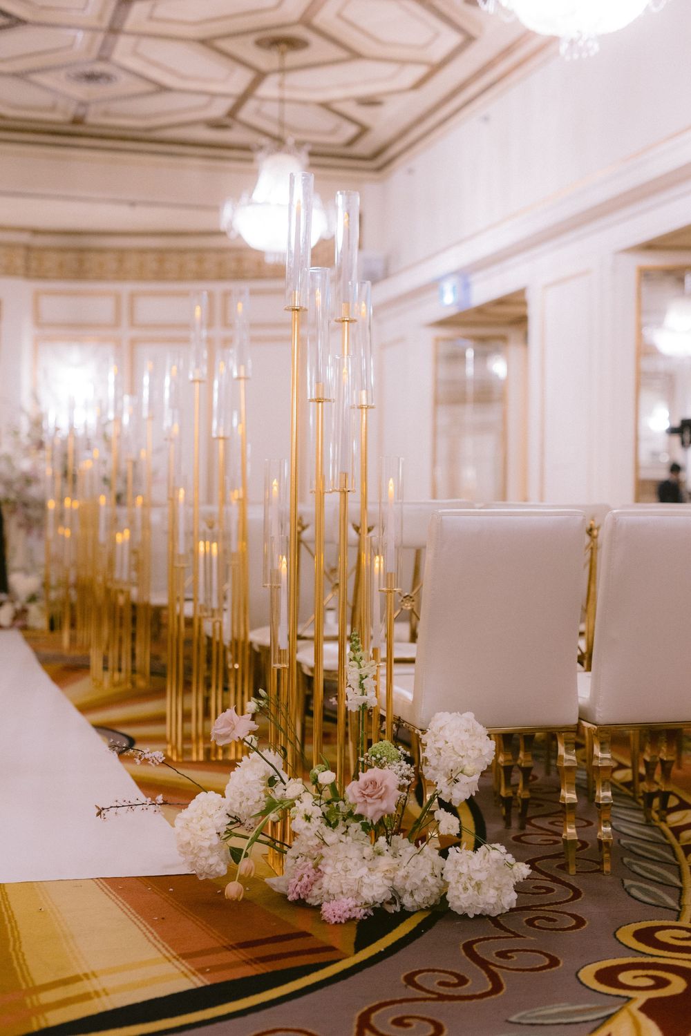 Elegant wedding reception tables adorned with tall gold candelabras and white floral centerpieces in a luxurious ballroom.