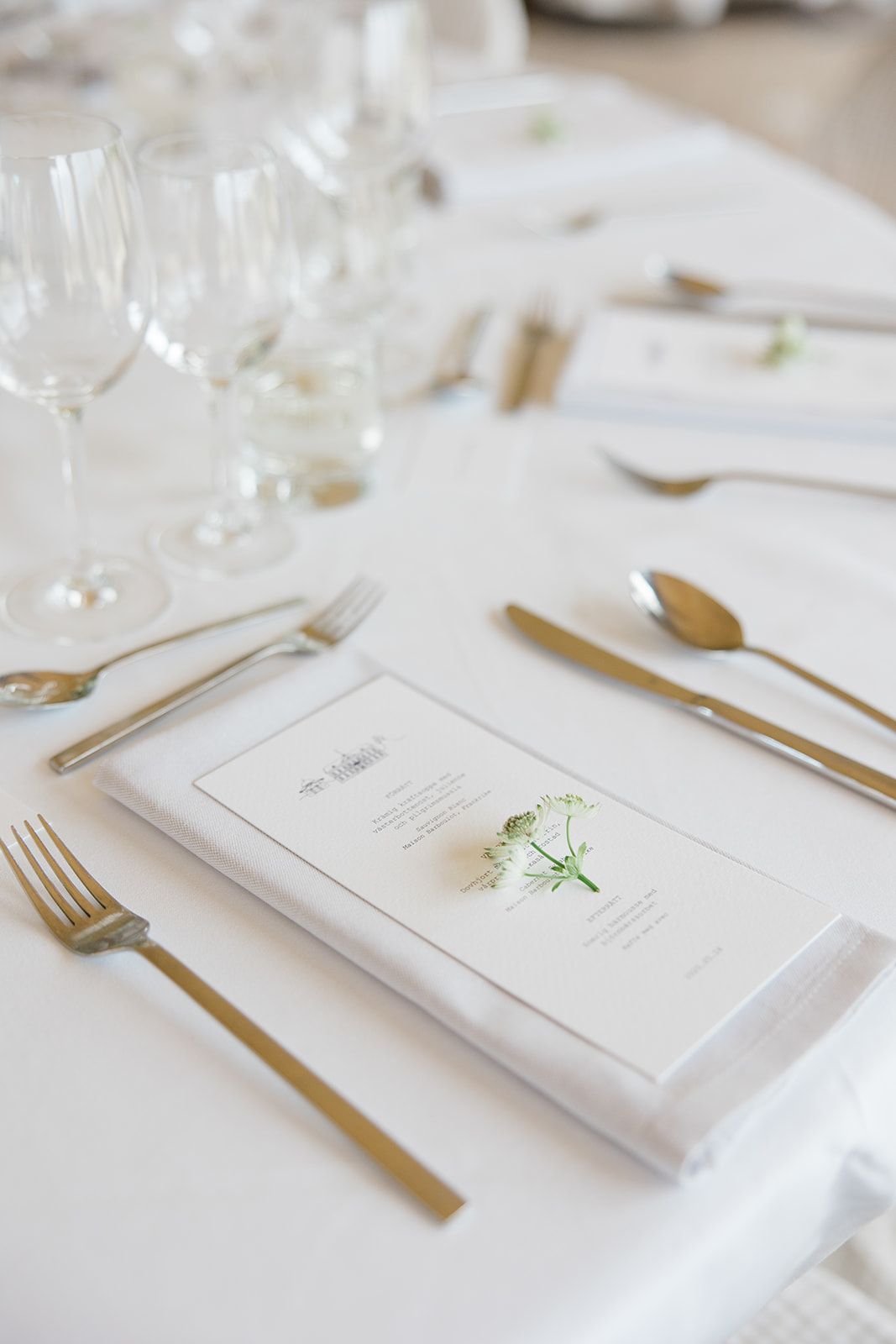 Elegant white table setting with gold cutlery, menu cards and delicate floral accents at a formal dining event.