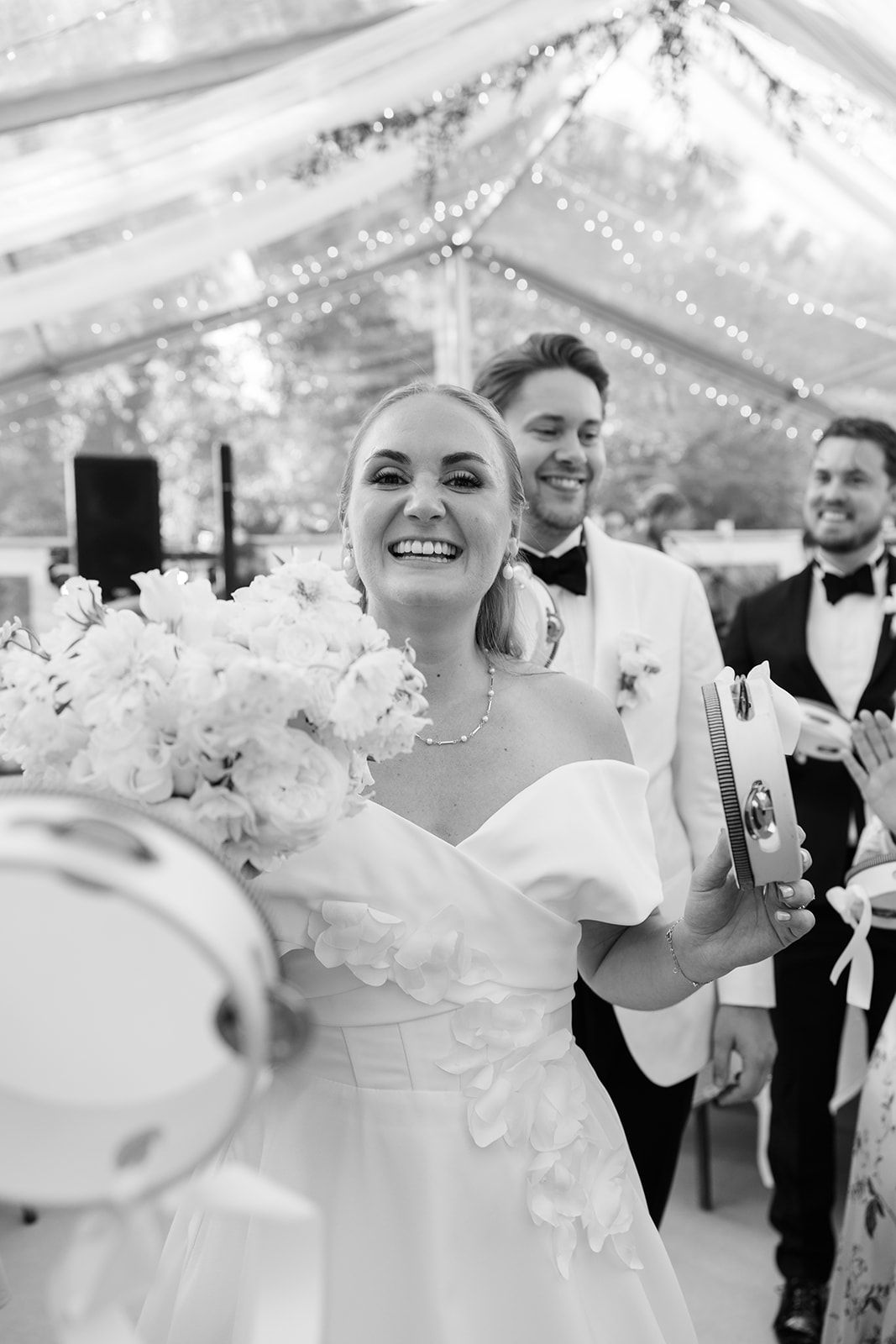Joyful wedding celebration moments captured in black and white under an elegant tent with string lights and floral decor.