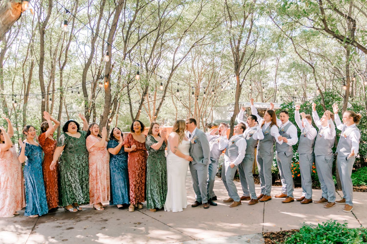 Large wedding party group photo with bridesmaids and groomsmen lined up against a natural green backdrop.