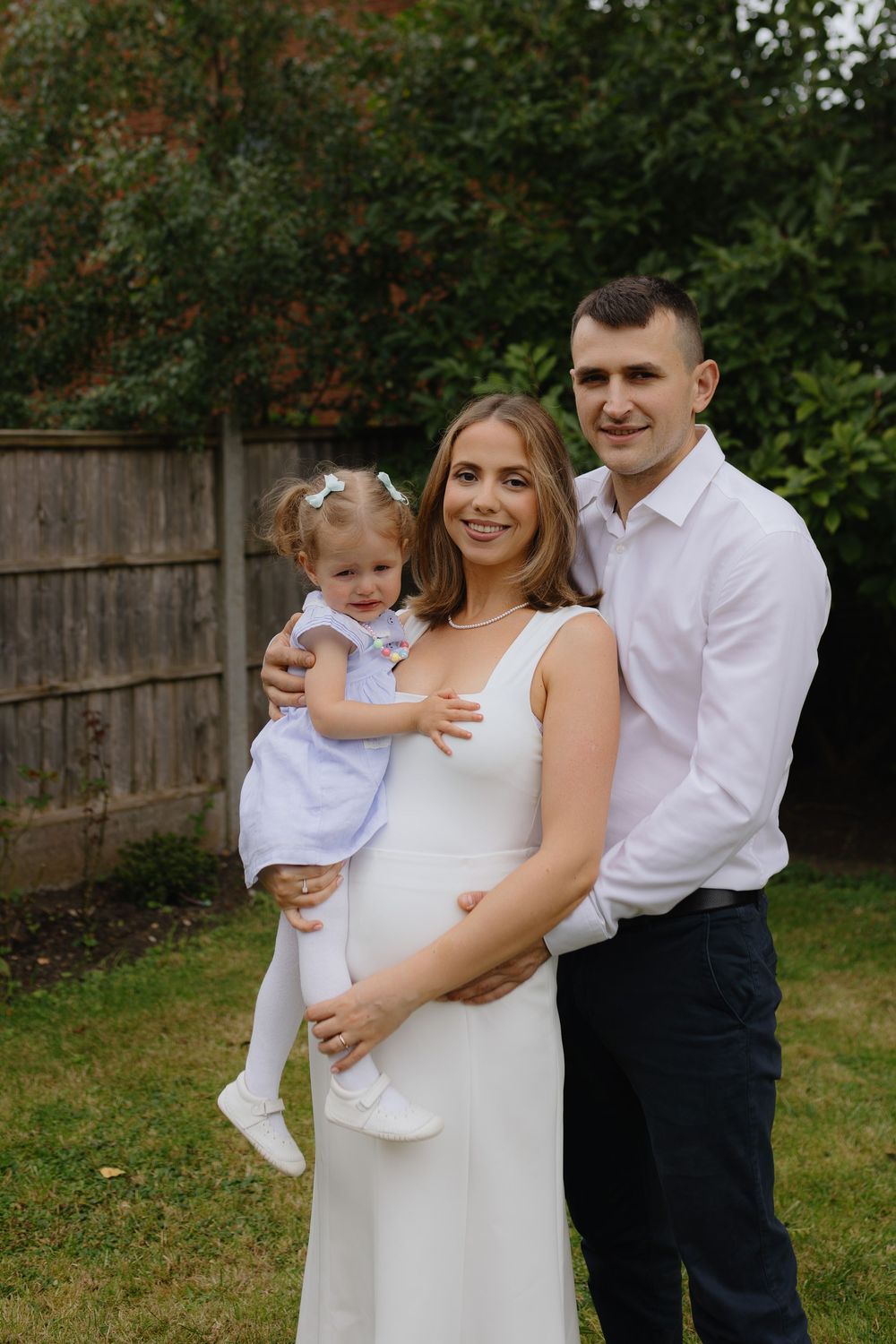 A family poses together in a backyard garden setting, with a white dress and formal attire.