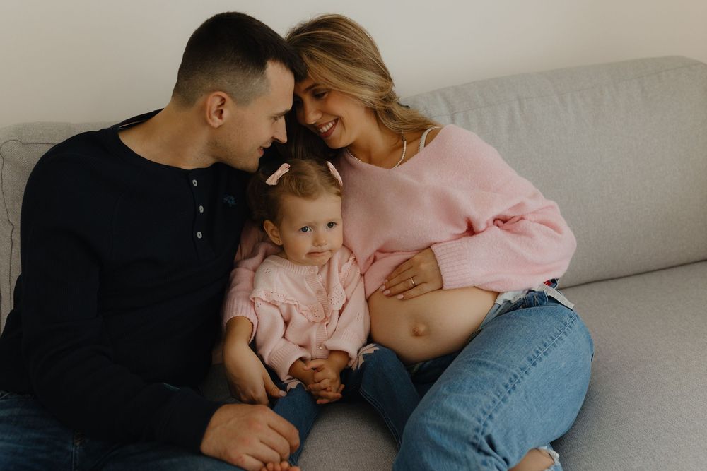 A series of intimate family moments showing parents cuddling with their baby on a couch in natural light.
