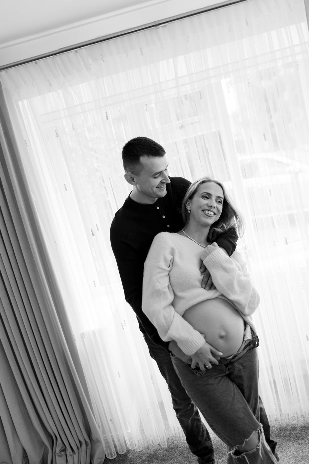Black and white maternity photos showing intimate moments between expectant parents near a window.