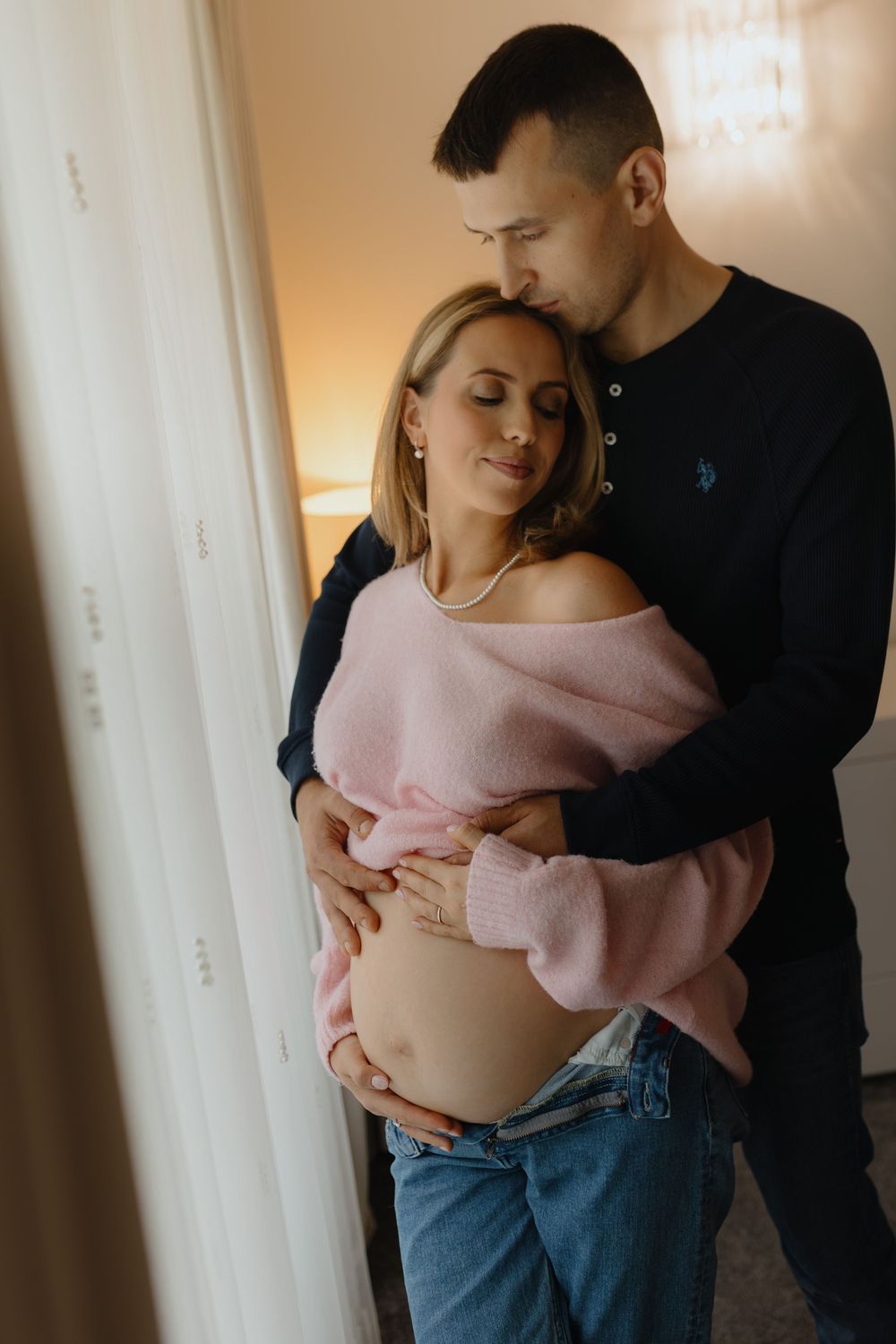 A couple embraces tenderly in a softly lit room with warm natural lighting.