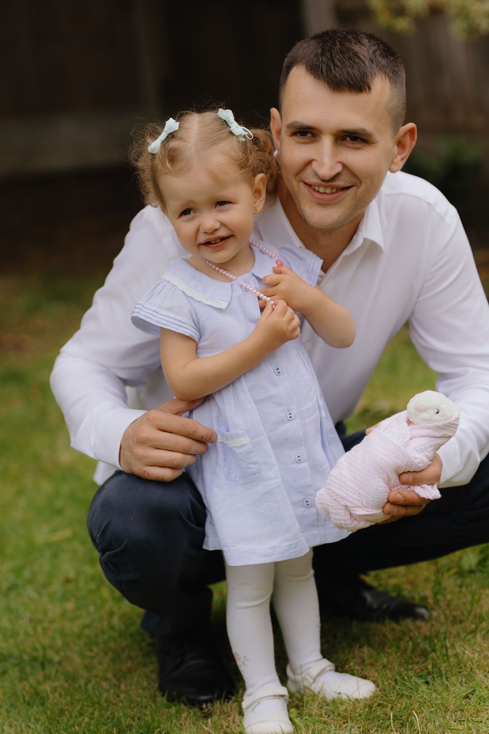 A sweet moment captured in white outfits as a child and adult share smiles and laughter on the grass outdoors.