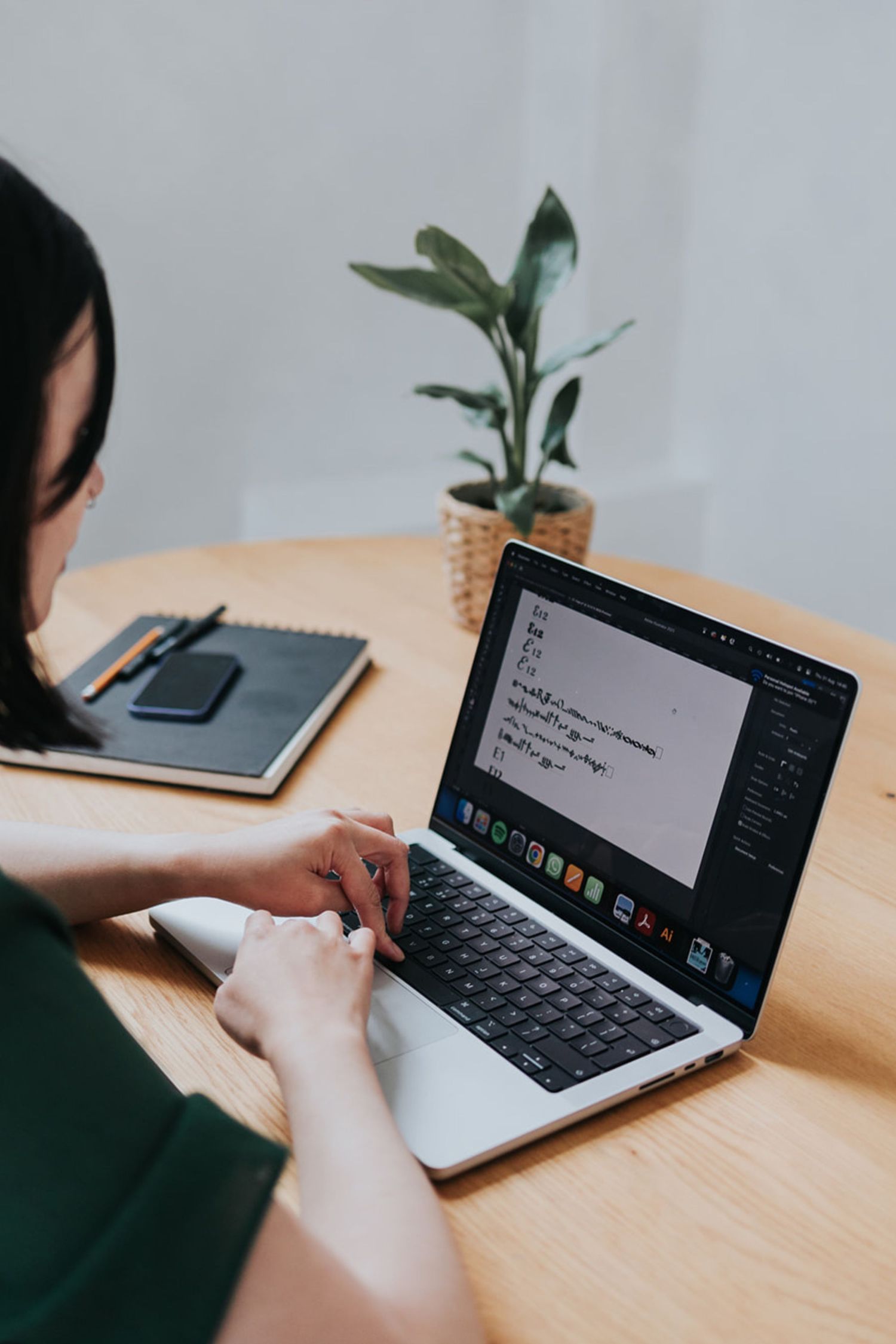A person working on a tablet device with keyboard attachment on a wooden desk surface in a minimalist setting.