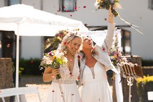 Outdoor wedding reception setup with white tents, tables and chairs decorated with floral arrangements and string lights.