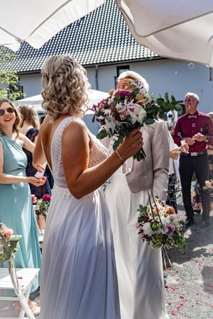 Wedding party members in light blue and white dresses hold bouquets while confetti falls around them during celebration.