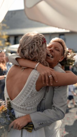 Two people share an emotional embrace at an outdoor wedding celebration while wearing formal attire.