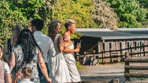 A group of people walk along a wooden boardwalk on a sunny day with trees in the background.