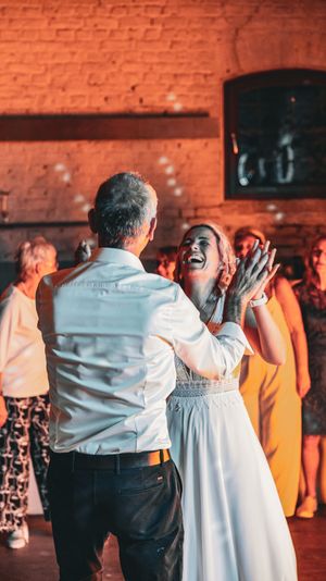 People dancing and celebrating at a wedding reception with exposed brick walls and warm lighting in the background.