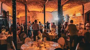 A panoramic view of a dimly lit rustic restaurant interior with brick walls and tables set for dining service.
