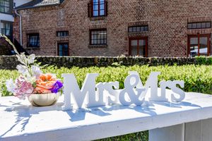 Wedding reception table setup with white decor and floral arrangements on a sunny day outdoors.