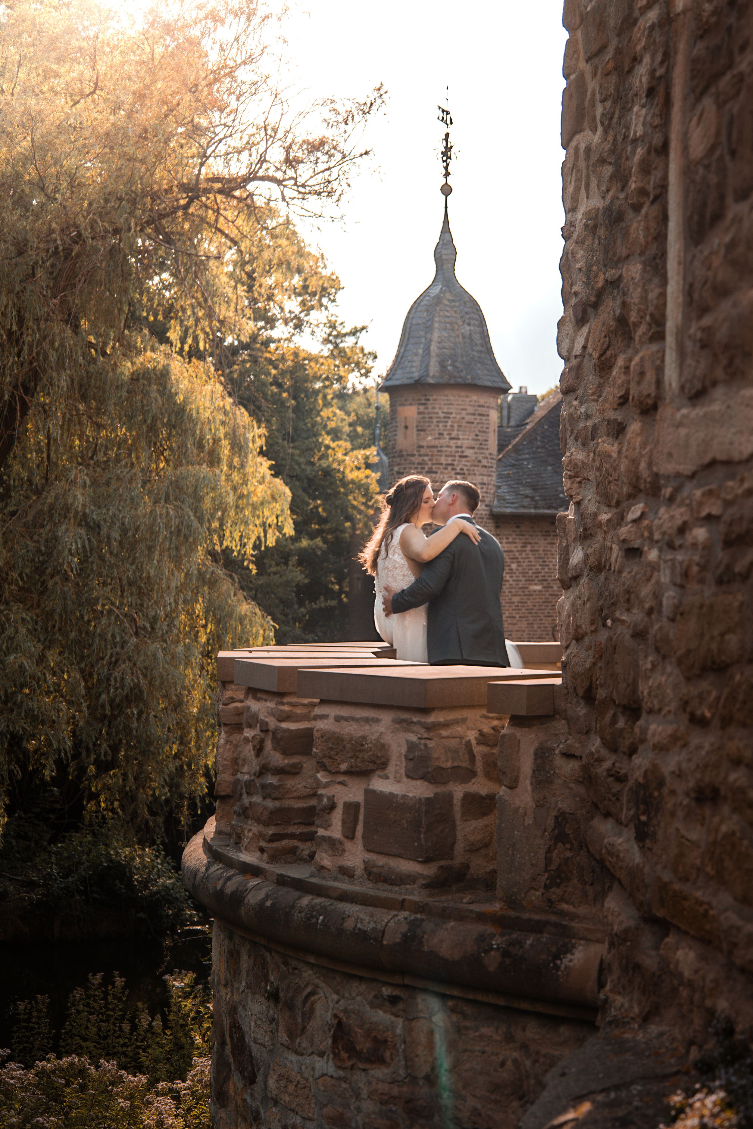 Person sits on stone wall of medieval castle ruins at sunset with church spires visible in background.