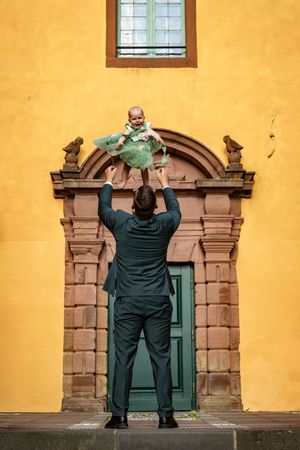 Person in green overalls stands in front of ornate stone doorway on yellow building wall.