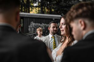 Wedding guests gathered outdoors during a ceremony with selective focus on a person wearing a yellow tie.