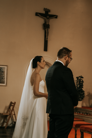 A bride and groom kneel before a crucifix at the altar during their Catholic church wedding ceremony.