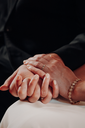 Two hands wearing delicate jewelry intertwined on a white surface in a romantic black and white composition.