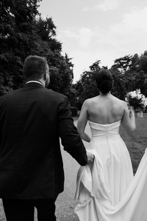 Artistic black and white wedding photos showing the back of a bride's dress while walking outdoors.