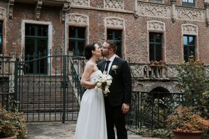Newlyweds embrace and laugh together outside a vintage brick building with iron gates.