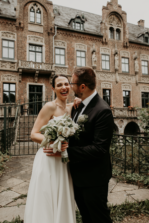 A joyful wedding couple shares an intimate moment in front of a historic brick building with ornate architecture.
