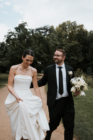 A playful moment between newlyweds as they walk together on a path with trees in the background.