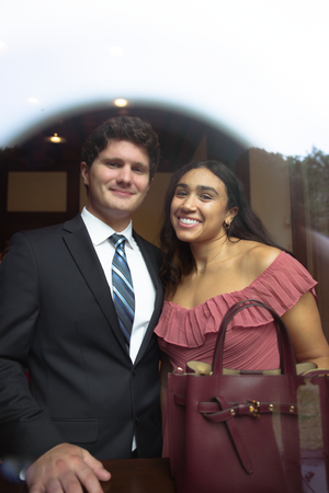 A couple poses together at a formal event, with the person in a burgundy ruffled dress holding a matching purse.