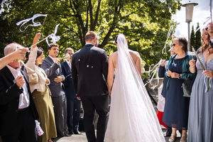 Outdoor wedding ceremony with guests gathered under trees on a sunny summer day.