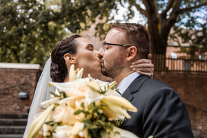 A romantic wedding portrait showing a couple embracing outdoors near a rustic brick wall.