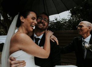 A couple shares a tender moment under a black umbrella during their wedding day.