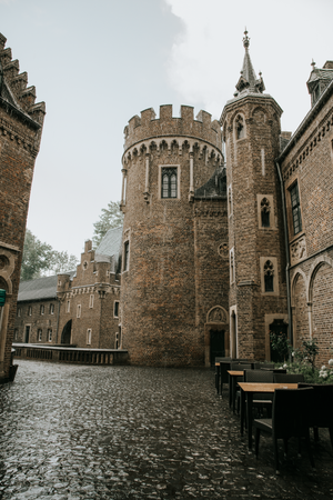 Historic castle courtyard with stone walls, turrets and cobblestone pavement on an overcast day.