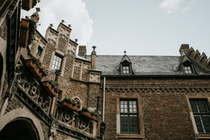 Historic brick buildings with ornate architectural details and arched windows line an old European street.